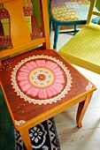 Seat of orange-painted wooden chair painted with pink and red floral motif in front of further colourful chairs
