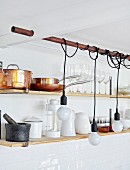 Bulb-style pendant lamps with cords wrapped around copper pipe in front of pans and glasses on wall-mounted shelves