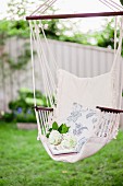 White hydrangea flowers and floral cushion in hanging chair in garden
