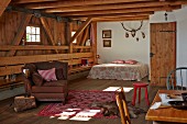 Offener Wohnraum mit Sitzmöbeln und Doppelbett in ländlichem Holzhaus