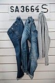 Jeans and jumper hanging from coat pegs on board wall