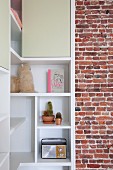 White, custom-made corner shelving with open compartments and cupboards adjoining unrendered brick wall