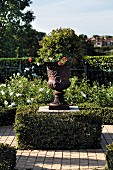 Planted classic urn on plinth surrounded by box hedge in sunny garden