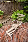 Holz-Gartenliegestuhl in rustikaler Gartenecke mit Bretterboden, Kies und Ziegelsteinboden
