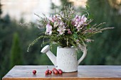 Autumn bouquet of heather, ivy and pink lilies in white ornamental watering can