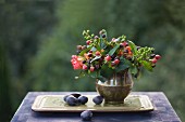Autumn still-life arrangement with posy of berries in brass vase and plums on tray