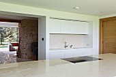 weiße schmale Einbauküche, Durchgang zum Wohnraum mit Natursteinkamin