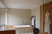 Mit Bodeneinbaustrahlern beleuchtete Badewanne vor gefliester Wand, Einbaustrahler in abgehängter Decke in elegantem, modernem Bad