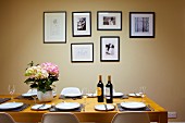 Wine bottles and hydrangea on set dining table in front of framed pictures on pastel wall
