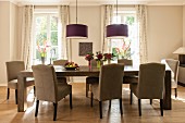 Elegant upholstered chairs around long, solid-wood table below pendant lamps in dining room
