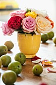 Vintage Vase mit Rosenstrauss, davor grüne Äpfel auf Holztisch