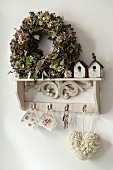 Wreath and vintage-style miniature nesting boxes on antique key rack with rose-patterned cups and love-heart pendant hanging from hooks