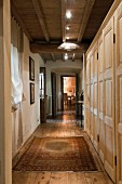 Pale, wooden custom cupboards and modern spotlights on wood-beamed ceiling in hallway