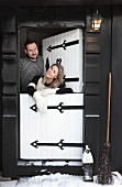 Young couple standing in white stable door of black wooden cabin