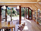 Essplatz vor offenen Terrassentüren mit Gartenblick, seitlich in sichtbarer Holzkonstruktion eingebaute Bücherregale