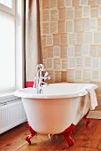 Vintage-style free-standing bathtub with red claw feet against patterned wallpaper