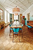 Long table, chairs with turquoise upholstery and pendant lamps suspended from diagonally panelled white ceiling in dining room