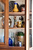 Collection of jugs, bottled and figurines in dresser with open glass door