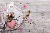 Pink heart-shaped ornament and posy of dried roses on vintage-style plate on rustic wooden surface scattered with flowers
