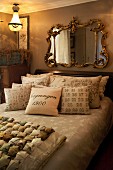 Collection of scatter cushions on French bed below Baroque mirror in ornate gilt frame in vintage-style bedroom