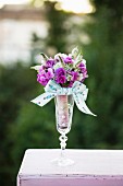 Festive posy of purple flowers and ribbon in glass vase outdoors