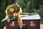 Festive bouquet of apricot roses and hydrangeas tied with ribbon on top of vintage suitcase
