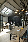 Dining table surrounding tree trunks, pendant lamp with wrought iron hoop and work stations in loft-style interior