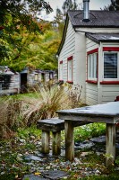 Rustikaler Tisch mit Bank in herbstlichem Garten, weisses Holzhaus im Hintergrund