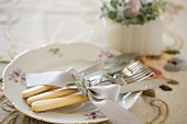 Vintage cutlery with cream plastic handles tied with ribbon on gold-rimmed plate