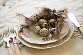 Quail eggs and feathers on floral gold-rimmed plate and vintage cutlery