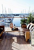 Outdoor furniture on sunny wooden terrace with yachting marina in background