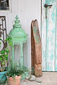 Arrangement of vintage candle lantern and weathered section of beam with printed motifs next to weathered, turquoise vintage door