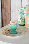 Boiled egg with top removed in turquoise eggcup in front of textile rabbit-shaped egg warmers