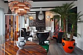 Runder Tisch unter Klassiker Pendelleuchte vor Loungebereich mit Retro Sesseln und Zimmerpalme in orangerotem Übertopf