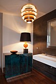 Table lamp on elegant sideboard, sink and retro pendant lamp in designer bathroom