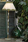 Vintage Stehleuchte mit Stoffschirm und grüne Ballonflasche neben Rankpflanze