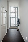 High-ceilinged narrow hallway with black-tiled floor, fitted cupboards with white sliding doors to one side and glazed house entrance at far end