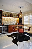 Retro chairs at round table with glass top on animal-skin rug in home bar with illuminated stone wall