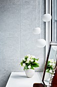 Vase of white flowers and dressing mirror on dressing table below pendant lamps