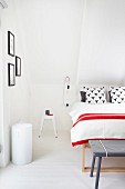 Bett mit rot-weiss gestreifter Tagesdecke, daneben Retro Hocker als Nachttisch im Dachgeschoss