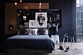 Dunkles Schlafzimmer mit Doppelbett vor Wand mit gerahmtem Spiegel und Bildern, 'Grunge'-Athmosphäre