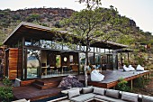 Modern safari lodge with glass façade and spacious wooden terrace in wild landscape