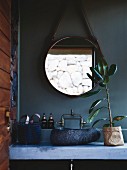Concrete washstand with stone basin below round mirror on petrol-blue wall