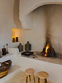 Two rustic wooden stools in front of open masonry fireplace with niches and platforms in restored Apulian trullo