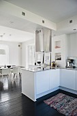 Open-plan white kitchen with counter and stainless steel extractor hood in front of dining area
