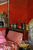 Vintage-style interior with red walls, red and white striped cushions on daybed and collection of colourful vases on side table