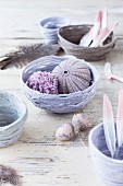Decorative arrangement of feathers, sea urchin tests and pompoms in hand-made yarn bowls