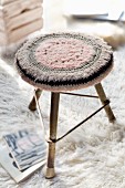 Crocheted seat cushion on three-legged stool on flokati rug