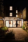Courtyard with paved area at night and view into modern extension with illuminated interior