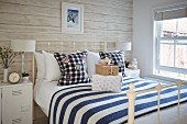 Double bed with white metal frame and white-and-blue striped bedspread in rustic bedroom